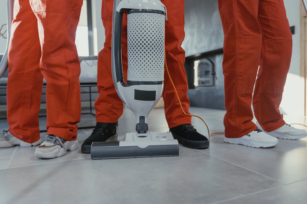 digital Team of professional cleaners in red uniforms using a vacuum cleaner indoors.